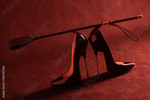 Black shiny high heel shoes and a whip on a dark background