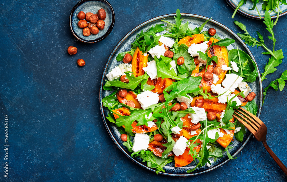 Fresh salad with grilled peach and feta cheese, hazelnuts and arugula on blue table background, top view, copy space Fresh salad with grilled peach and feta cheese, hazelnuts and arugula on blue table background, top view, copy space