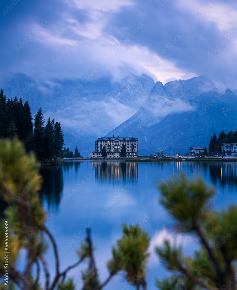 Fototapeta premium See mit Spiegelung und Bergmassiv mit Wolken im Hintergrund.