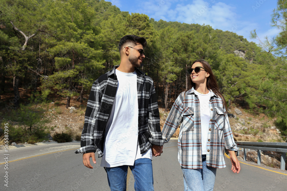 Romantic scene with happy hipster couple in checked flannel shirts walking down the empty switchback road. Young people holding hands. Close up, copy space, background. Romantic scene with happy hipster couple in checked flannel shirts walking down the empty switchback road. Young people holding hands. Close up, copy space, background.