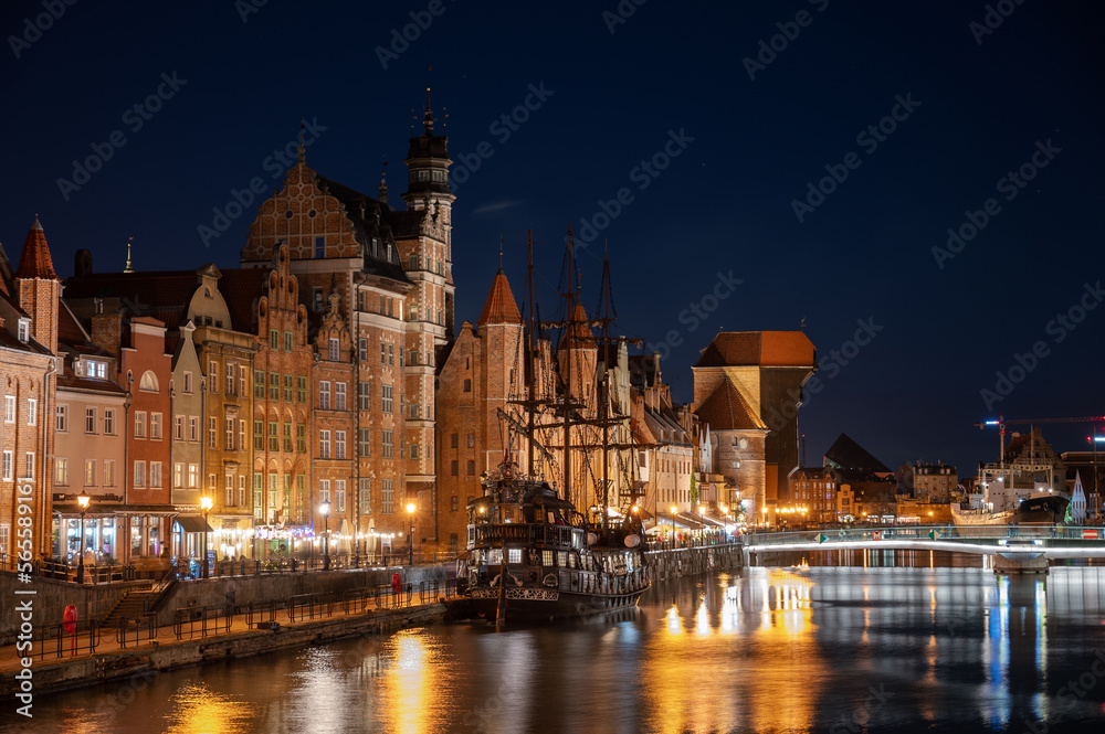 Night image of the river and the buildings of the city of Gdansk (Poland) illuminated, capturing the reflection of the water with a medieval ship.