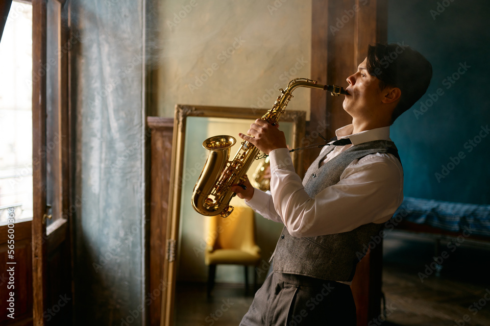 Young elegant man playing gold alto saxophone in misty room - obrazy, fototapety, plakaty 