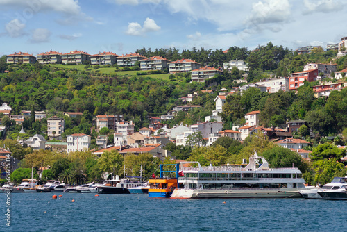 View from the sea of the green mountains of the Europian side of Bosphorus strait, with docked boats, traditional houses and dense trees in a summer day © Khaled El-Adawi