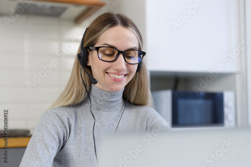 Friendly call center operator in headset speaking with client with a smile. Cheerful young woman from online support team talks to customer on a phone call photo
