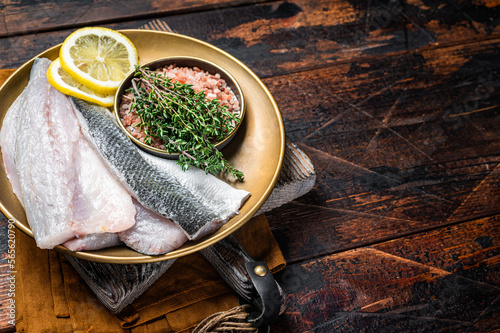 Uncooked Raw Sea Bass fillets, Seabass fish with thyme, pink salt and lemon. Dark background. Top view. Copy space photo