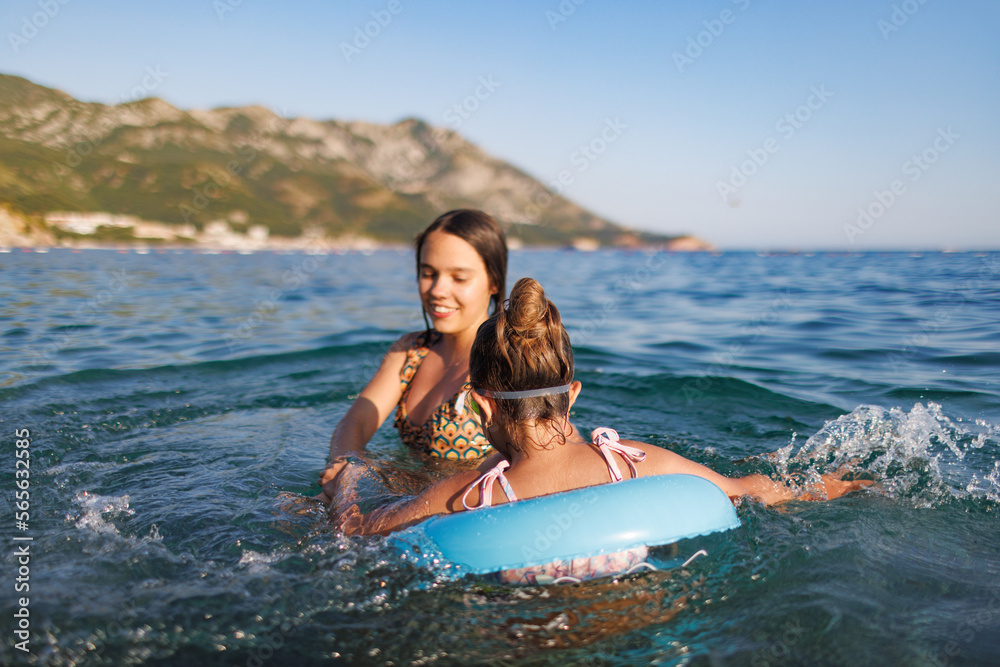 Two sisters in bathing suits play with an inflatable ring in the sea Two sisters in bathing suits play with an inflatable ring in the sea