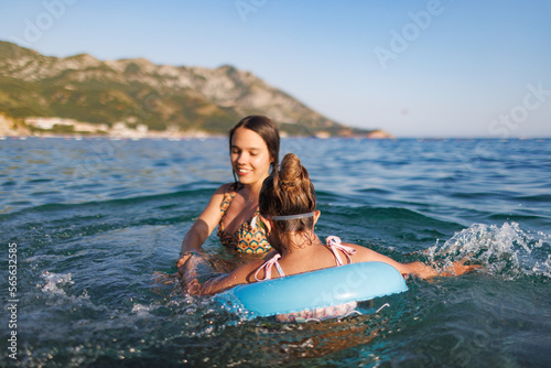 Two sisters in bathing suits play with an inflatable ring in the sea © YouraPechkin