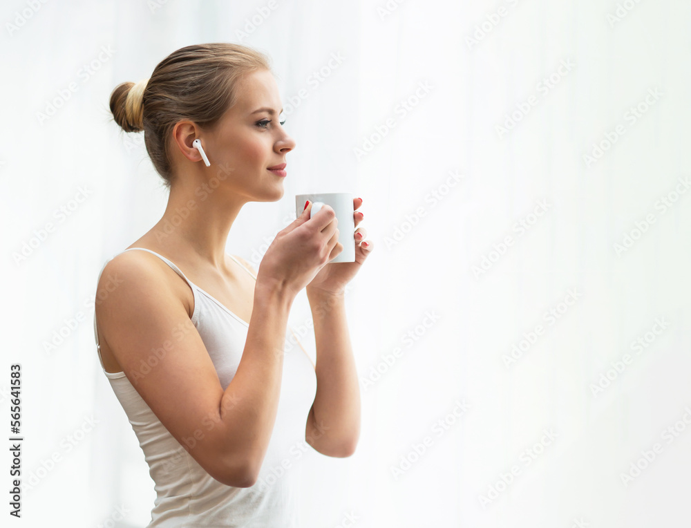 Young woman in white underwear is standing in front of the window and looking into it. Girl at home in the living room. Young woman in white underwear is standing in front of the window and looking into it. Girl at home in the living room.