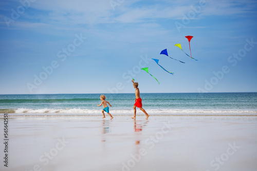 Boys run holding many colorful kite at beach smiling side view