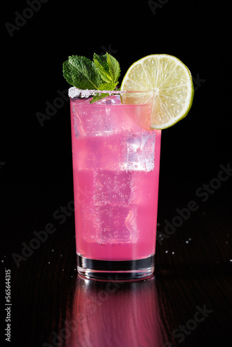 Pink lemonade with ice and decoration of mint and lime slices on a black background. Side view, selective focus.