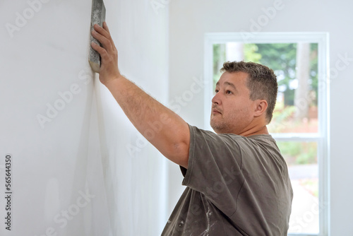 Worker sanding drywall mud in room during renovation of house with use sand trowel