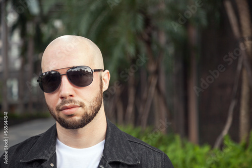 Cool confident young guy in sunglasses wearing a jacket. Bald and bearded macho man radiating success
