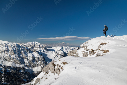 person with skis standing at the edge of a cliff in mountains in winter
