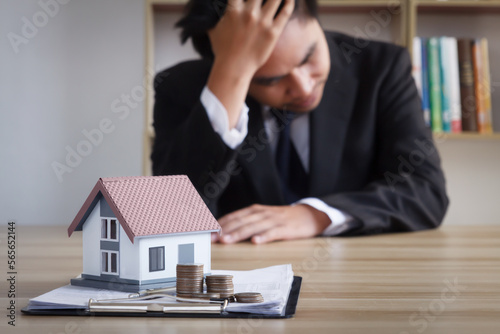 Young businessman sits depressed with a model of a house in front of him, the concept of real estate debt spreading around the world.  rising interest rates  world economic crisis photo