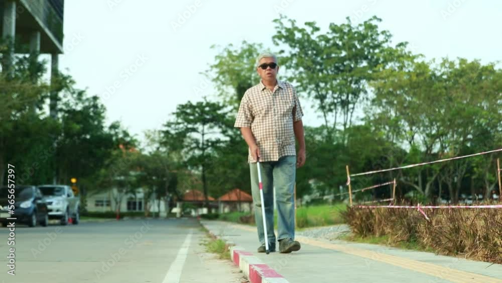 Elderly blind asian man using wearing sunglasses a cane for the blind walks on the sidewalk with caution without causing trouble to others. Elderly blind asian man using wearing sunglasses a cane for the blind walks on the sidewalk with caution without causing trouble to others.