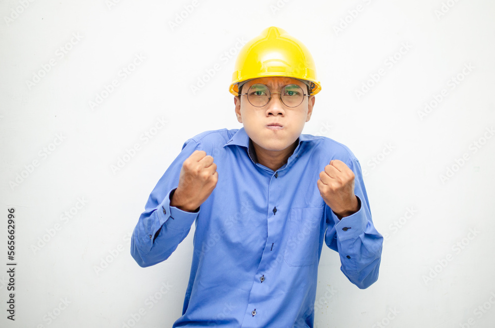 asian male construction worker or engineer in blue shirt and safety yellow helmet shows expresion of anger, furious and dissapointment isolated over white. stressed over work concept asian male construction worker or engineer in blue shirt and safety yellow helmet shows expresion of anger, furious and dissapointment isolated over white. stressed over work concept