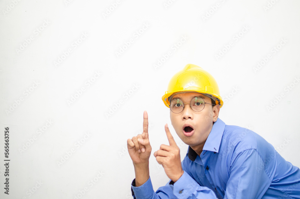 side view of A happy, shocked asian consrtuction worker in blue shirt and yellow safety helmet pointing finger and presenting something ads. 