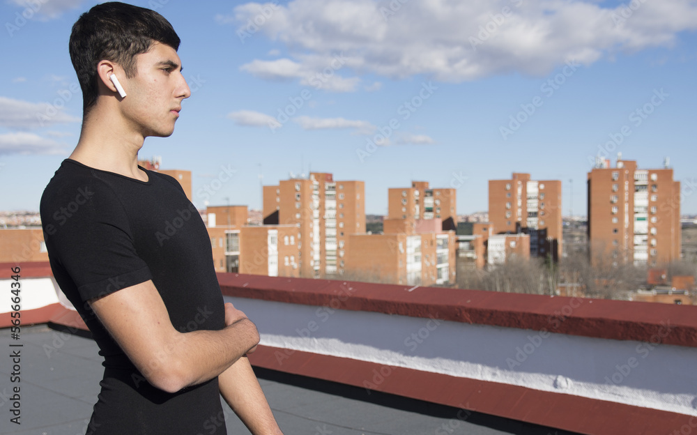 Fototapeta premium Strong sporty sportsman in sport clothes warm up training do stretch exercise on a roof listening to music