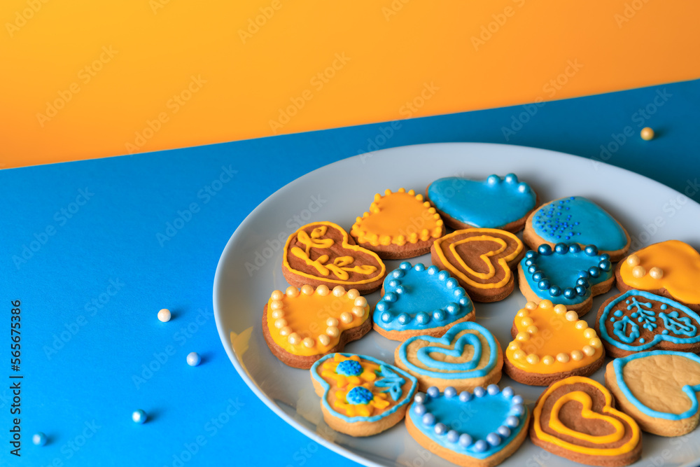 Cookies in shape of hearts decorated by yellow and blue icing and sprinkles on blue plate on blue table against yellow background Cookies in shape of hearts decorated by yellow and blue icing and sprinkles on blue plate on blue table against yellow background