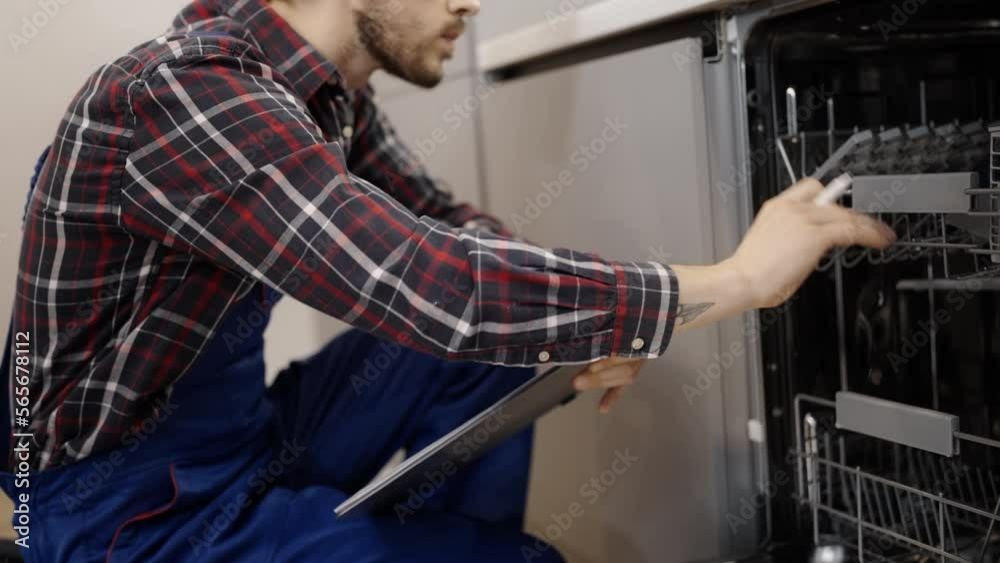 Closeup of man in uniform checking dishwasher, plumber occupation, maintenance Closeup of man in uniform checking dishwasher, plumber occupation, maintenance
