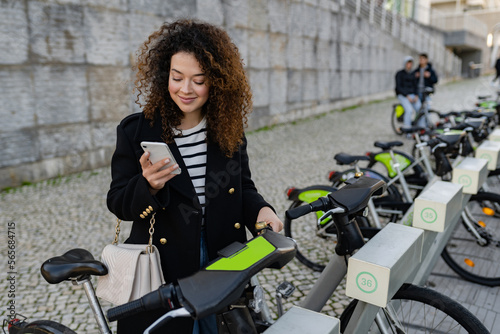 pretty curly woman renting a bicycle in street with an app