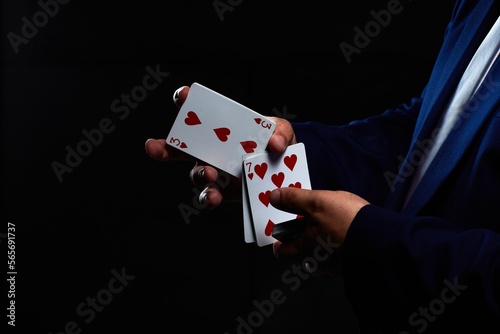 Magician illusionist showing performing card trick. Close up of hand and poker cards on black background. photo