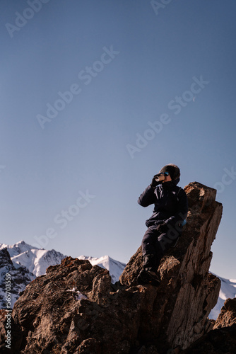 the guy drinks coffee sitting on a stone high in the mountains