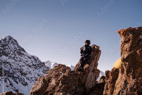 the guy leaned on a rock high in the mountains and drinks a drink from a paper cup