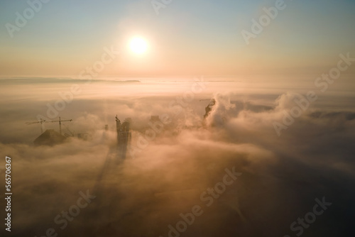 Aerial view of cement factory with high concrete plant structure and tower crane at industrial manufacturing site on foggy evening. Production and global industry concept © bilanol
