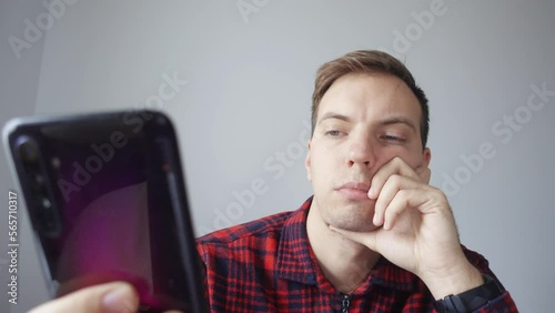 Portrait of a young young man use his phone during a business video conference with colleagues. His name is, he hides the phone, answers questions. View from the laptop webcam.