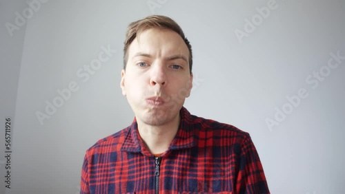 A young man eats a sandwich and drinks tea from a white cup in front of a laptop webcam during a video call, conference. View from the laptop webcam. High quality 4k footage