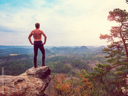 Shirtless hiker hold arms as akimbo at end of rocky cliff. Half naked man