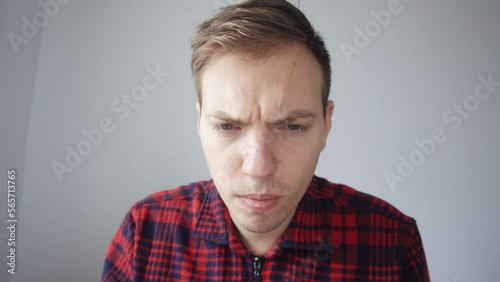 The young man peers at the screen. View from the laptop webcam. The man is looking at something on the monitor screen. He doesn't like what he sees. Blank white background. High quality 4k footage