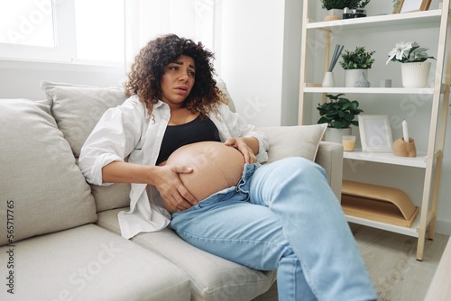 Pregnant woman headache lies at home in a shirt and jeans on the couch fatigue and heaviness in the last month of pregnancy before childbirth, lifestyle difficulties of motherhood, nausea