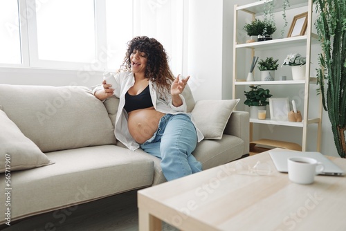 Pregnant woman smile blogger takes vitamins and medicines sitting on the couch at home freelancer in the last month of pregnancy lifestyle before childbirth