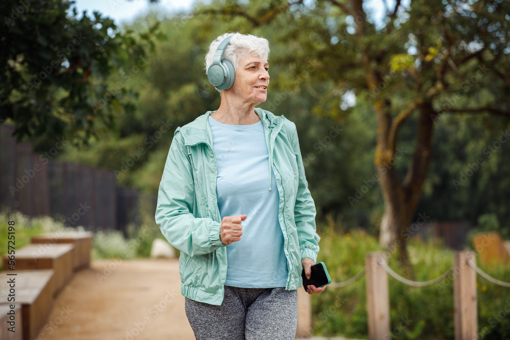 An elderly woman with a short haircut dressed in sportswear is jogging in the park while listening to music. An elderly woman with a short haircut dressed in sportswear is jogging in the park while listening to music.