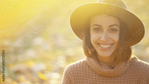 close up autumn portrait of beautiful smiling woman wearing in wrown dress, sweater and hat. girl holds yellow leaves and playfuly looking at camera photo