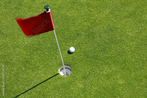 Close up shot of red golf flag and golf ball on golf course putting green shot from above.