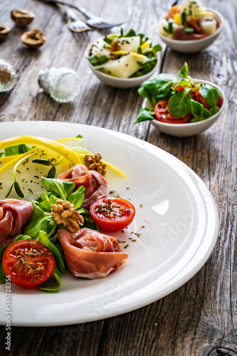 Tasty salad - prosciutto crudo, melon and fresh vegetables on wooden table 