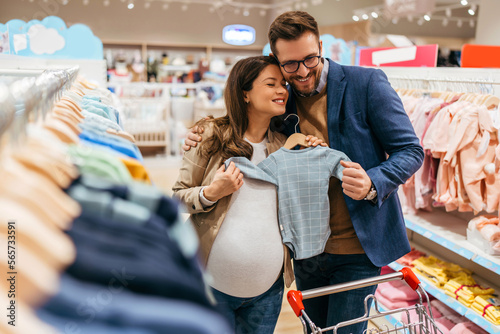 Attractive middle age couple enjoying in buying clothes and appliances for their new baby. Heterosexual couple in baby shop or store. Expecting baby concept.