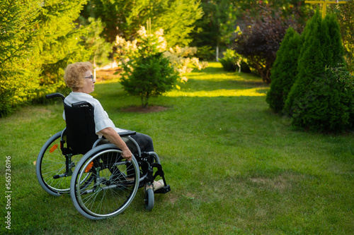 Happy elderly woman sitting in a wheelchair on a walk outdoors.  © Михаил Решетников