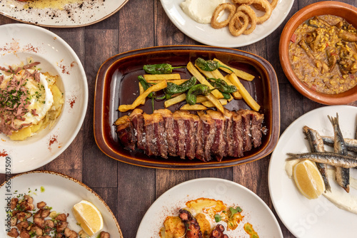 Set of dishes and tapas of Spanish gastronomy with sliced grilled beef entrecote with french fries, Galician octopus, fried anchovies, fried calamari, rice with partridge