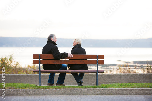 Rear view of mature couple sitting on bench overlooking river in Autumn.  © Pierre