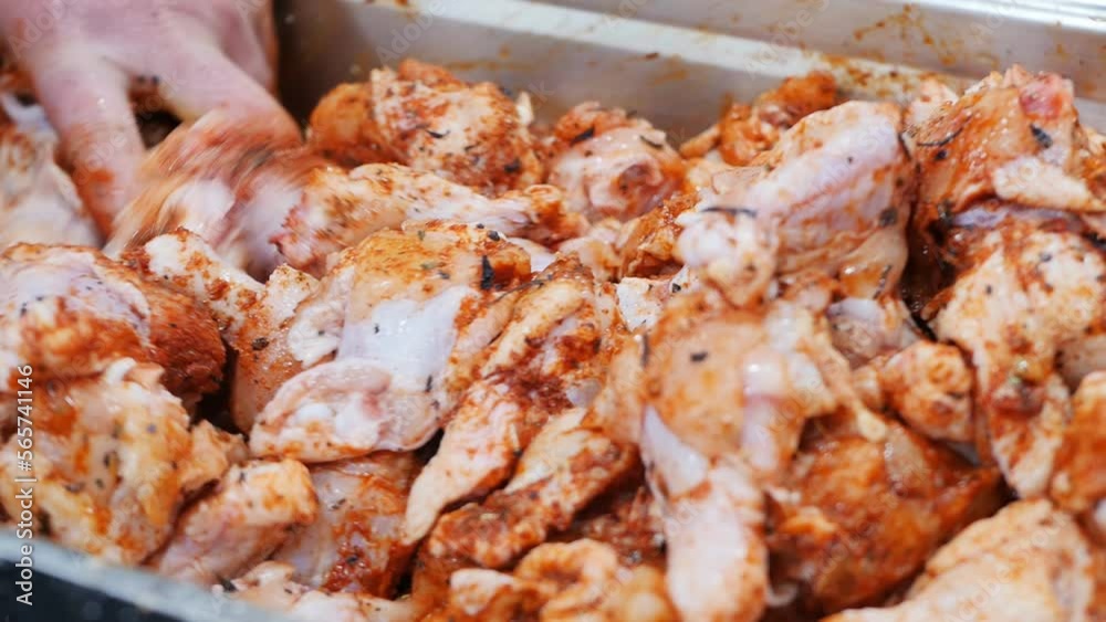 Close-up of the process of kneading chicken wings marinated with red paprika and hot peppers with basil with the bare hands of a cook in a metal container for frying delicious juicy wings. Fast food Close-up of the process of kneading chicken wings marinated with red paprika and hot peppers with basil with the bare hands of a cook in a metal container for frying delicious juicy wings. Fast food
