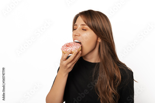 Young blonde woman with eyes closed is eating a fresh tasty pink doughnut.