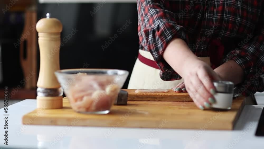 Woman's hands sprinkling raw chicken fillet with frtesh pepper om the wooden cutting desk. Slow motion. Woman's hands sprinkling raw chicken fillet with frtesh pepper om the wooden cutting desk. Slow motion.