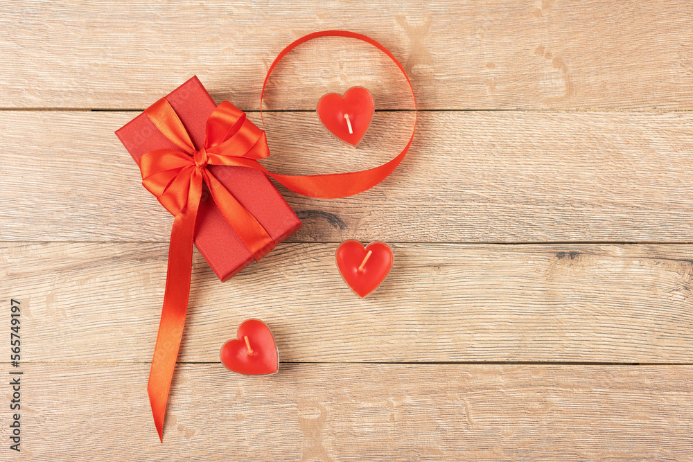 Red gift box with a red satin ribbon bow with red candles in the shape of hearts on a wooden background. Happy Valentine's Day, Mother's Day and birthday greeting card. Red gift box with a red satin ribbon bow with red candles in the shape of hearts on a wooden background. Happy Valentine's Day, Mother's Day and birthday greeting card.