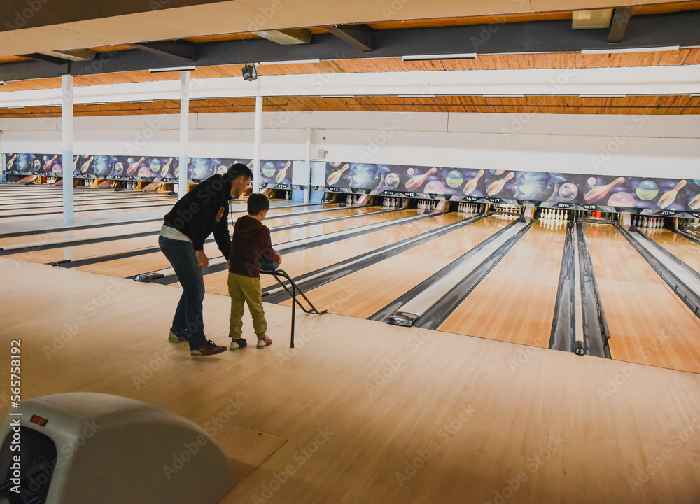 Father helping child roll bowling ball down a ramp at bowling alley ...