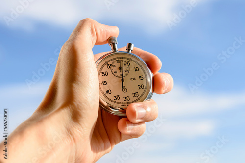 Cropped hand of man holding stopwatch against sky