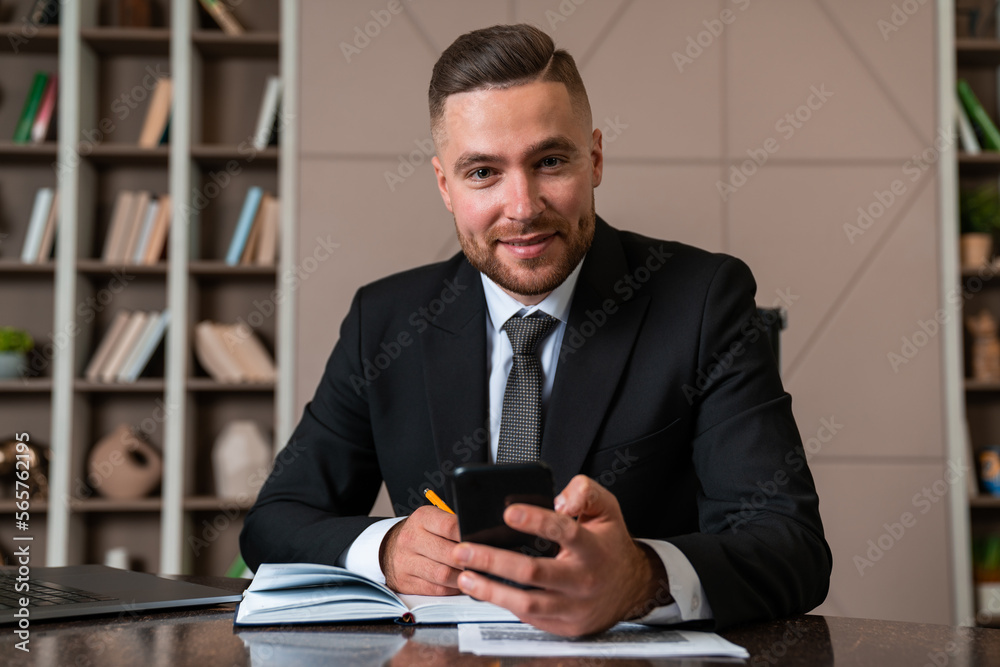 Smiling businessman sitting with smartphone in hand and taking notes Smiling businessman sitting with smartphone in hand and taking notes